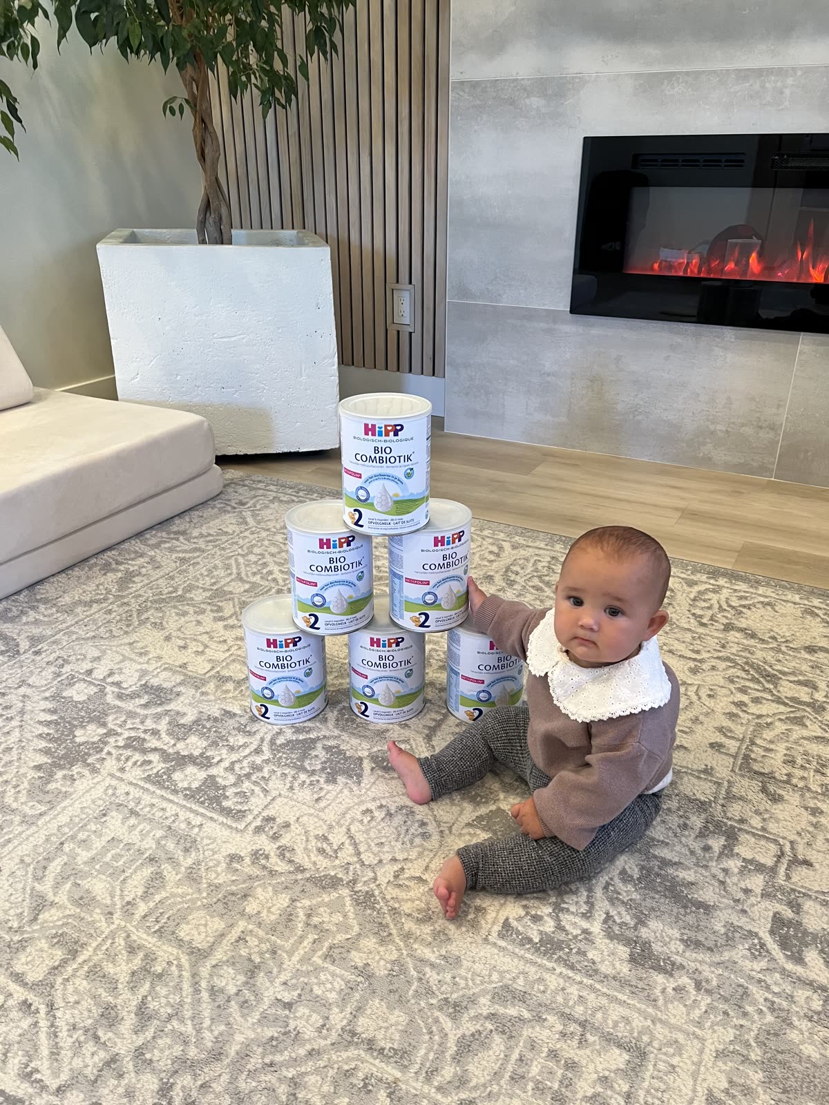 Kseniia's youngest sitting on the rug with three cans of HiPP Dutch